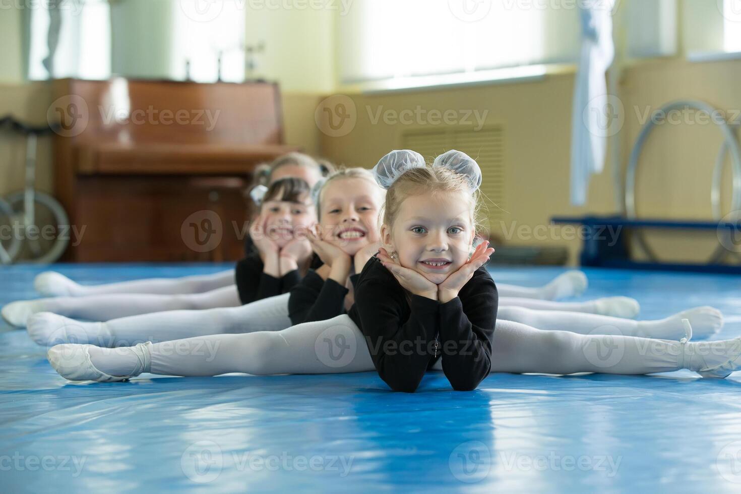 pequeño muchachas gimnastas sentar en el divisiones. niños hacer físico ejercicio. joven bailarinas.. formación de el inicial grupo en gimnasia.acrobacia lección foto