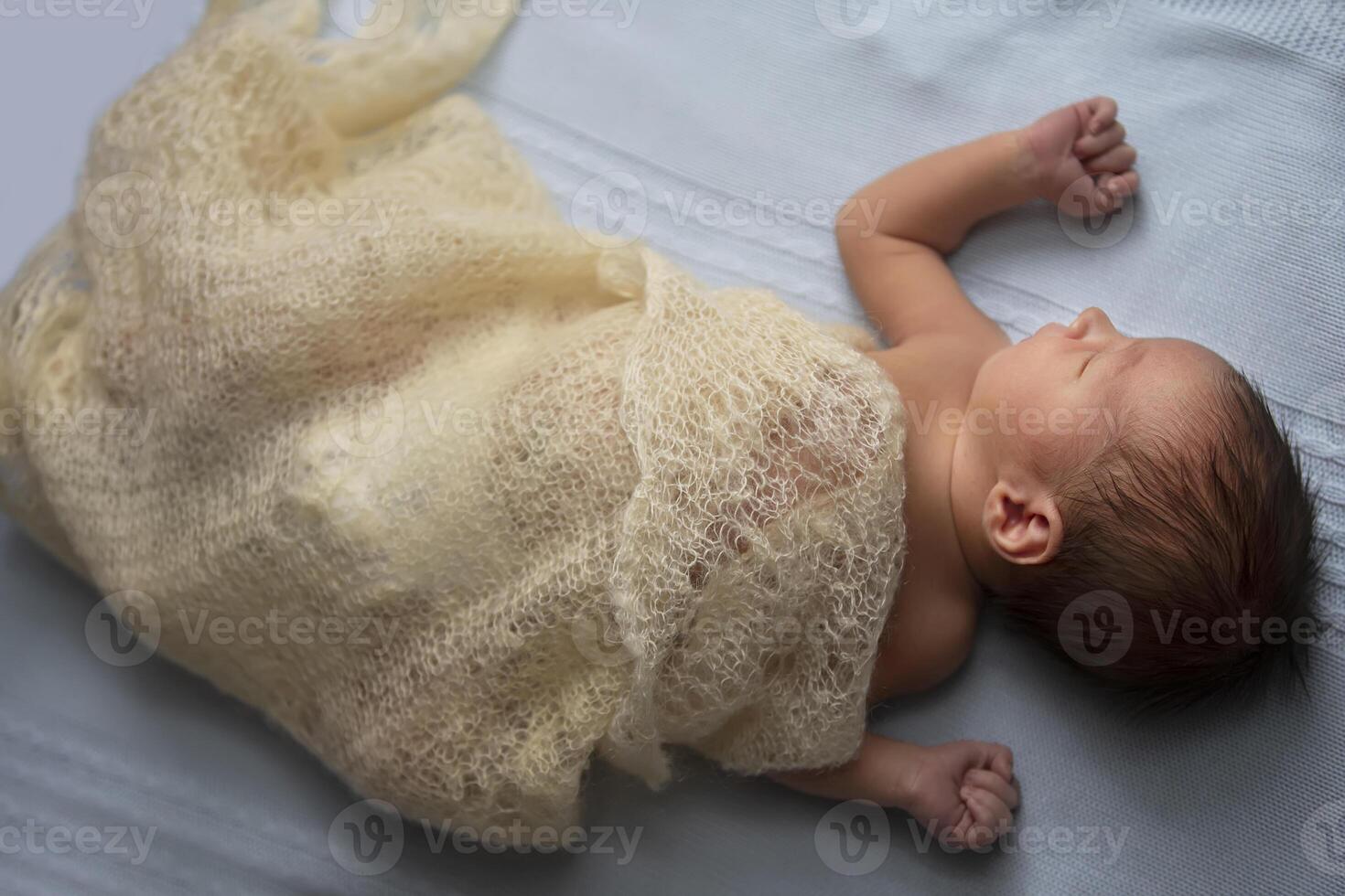 Newborn baby wrapped in a knitted blanket on a light background. photo