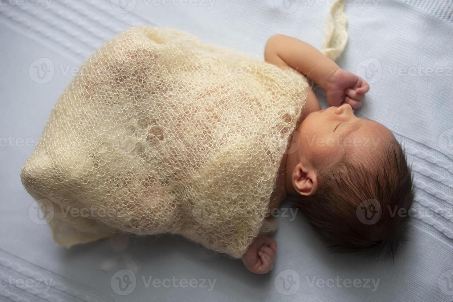 Newborn baby wrapped in a knitted blanket on a light background. photo