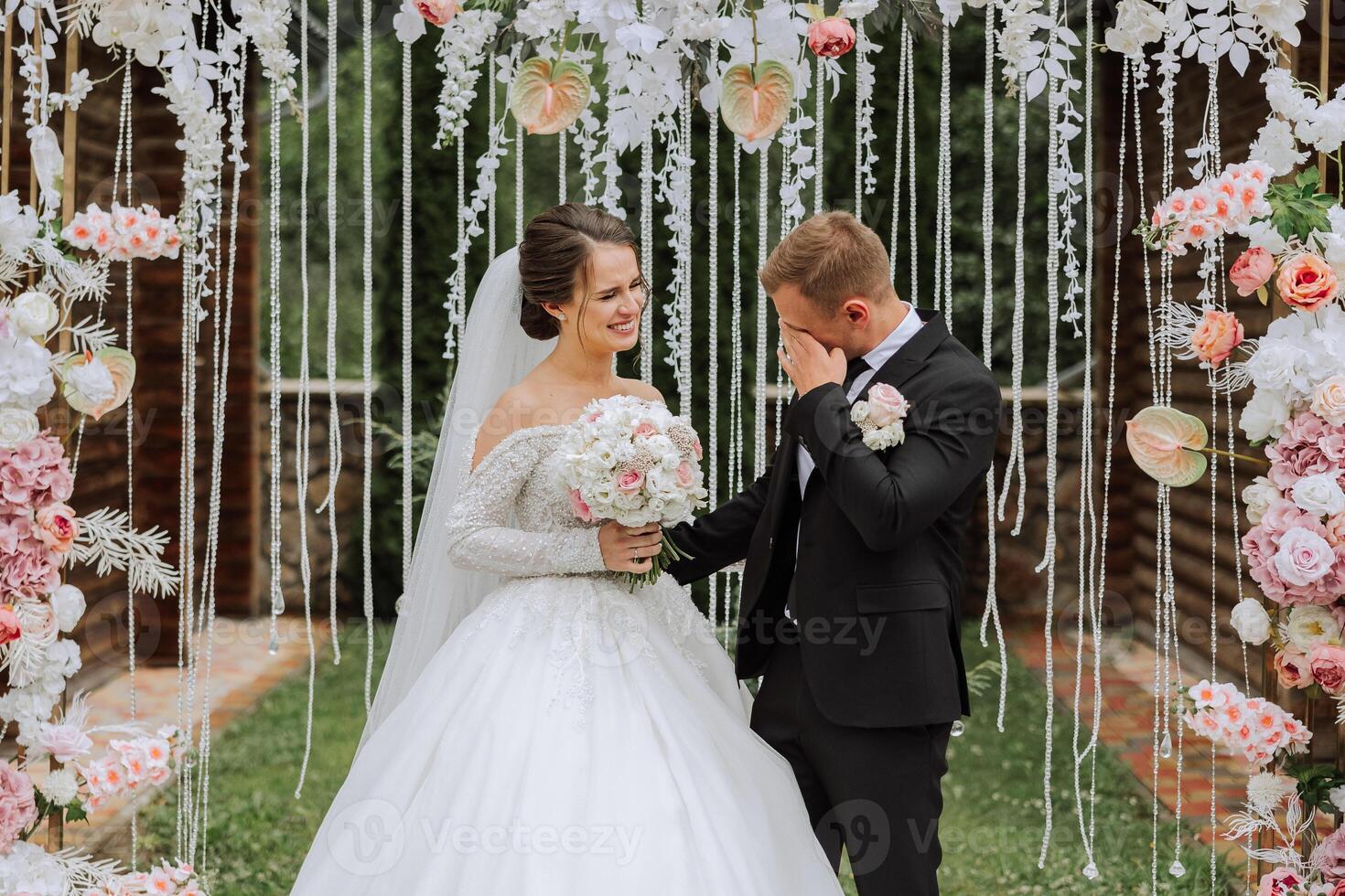 el novio llantos durante el Boda ceremonia cerca el flor arco. verano Boda en naturaleza. ella dijo Sí. un conmovedor momento a el Boda ceremonia foto