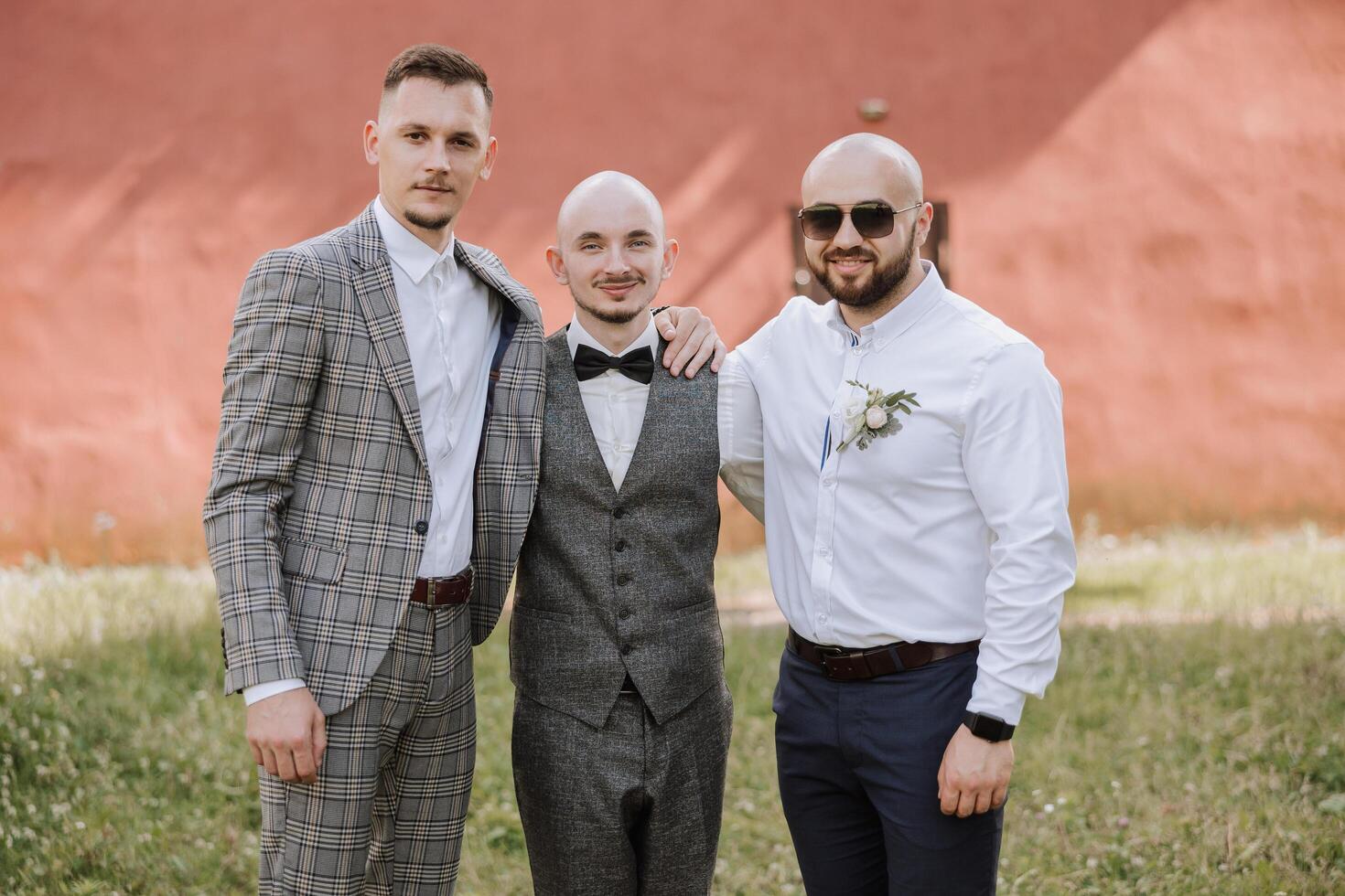 Cheerful, young, energetic witnesses of the groom next to the groom. Friends congratulate the groom. The groom in a vest and his friends in white shirts pose near the wedding arch. Wedding in nature. photo