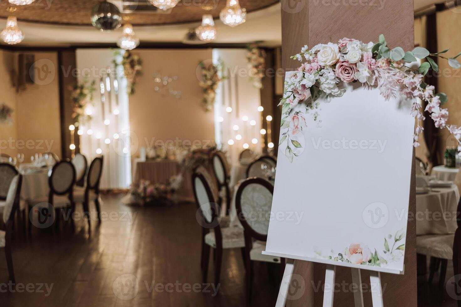 An original floral decorated board with a white sheet, against the backdrop of a deserted wedding hall in the background. with an inscription plate. photo