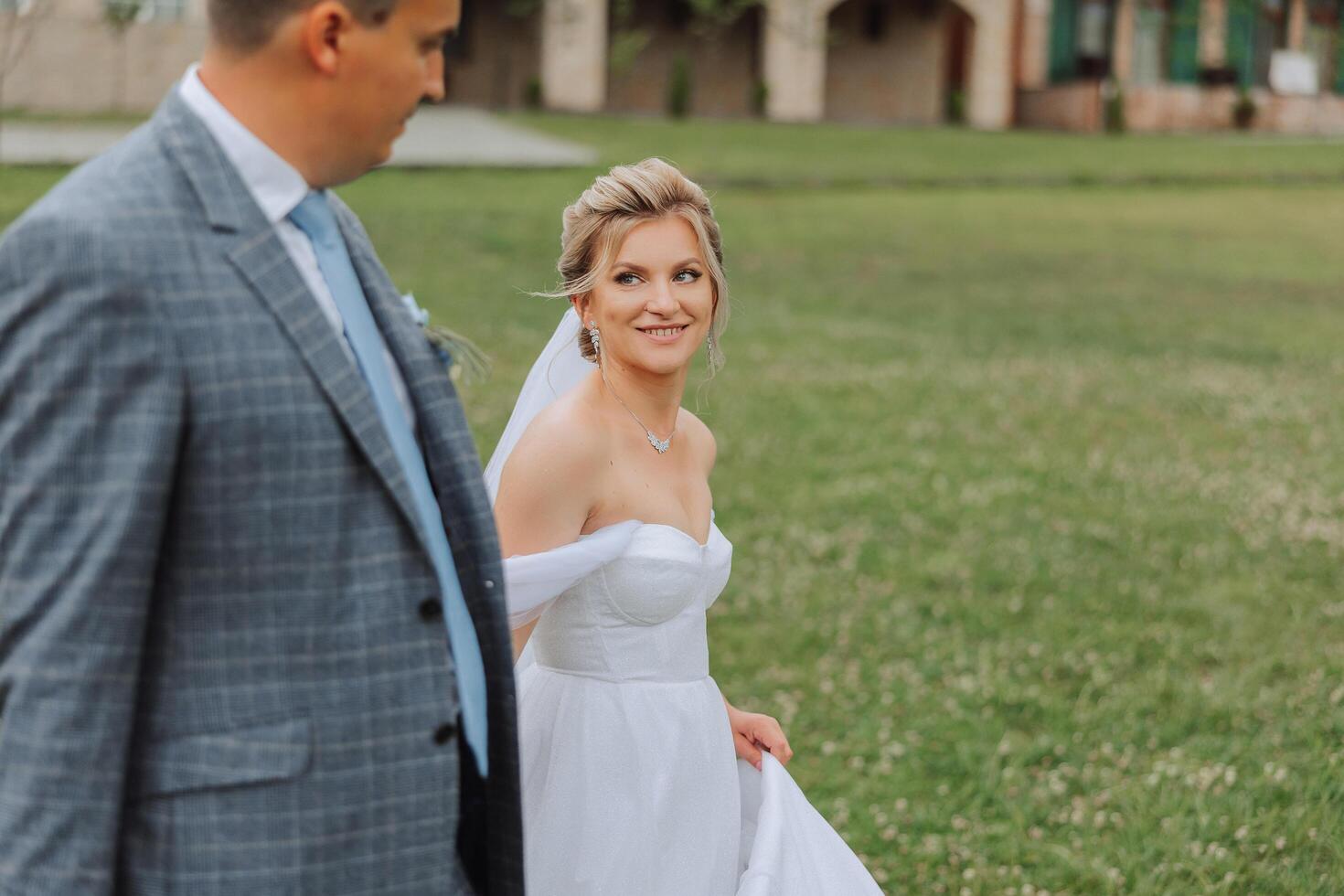 A handsome groom and an elegant bride in a lush white dress are walking in a summer park. Happy bride and groom getting ready for their best day. photo