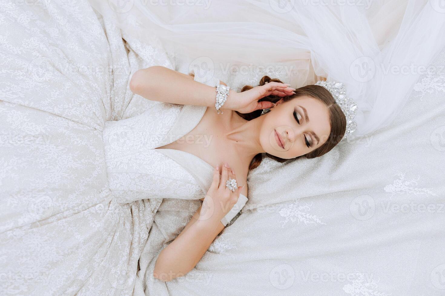 A beautiful bride in a white dress is lying. A girl in a white dress is resting. Beautiful hair and makeup. The model poses for the photographer. photo