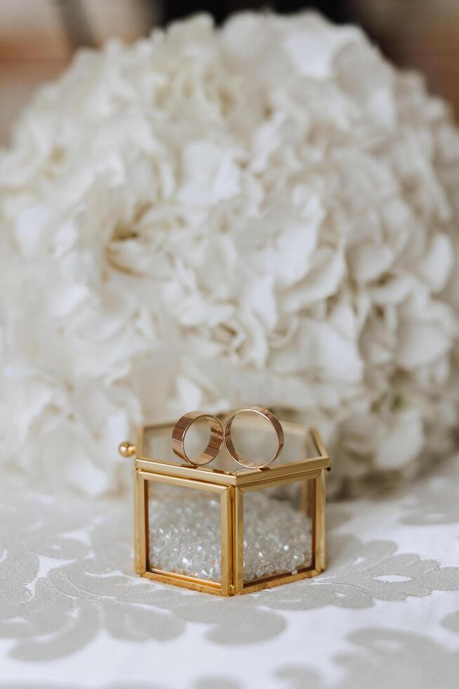 Wedding bouquet. White cut roses, green seed heads and leaves. Green stems and white ribbon and gold wedding rings. photo