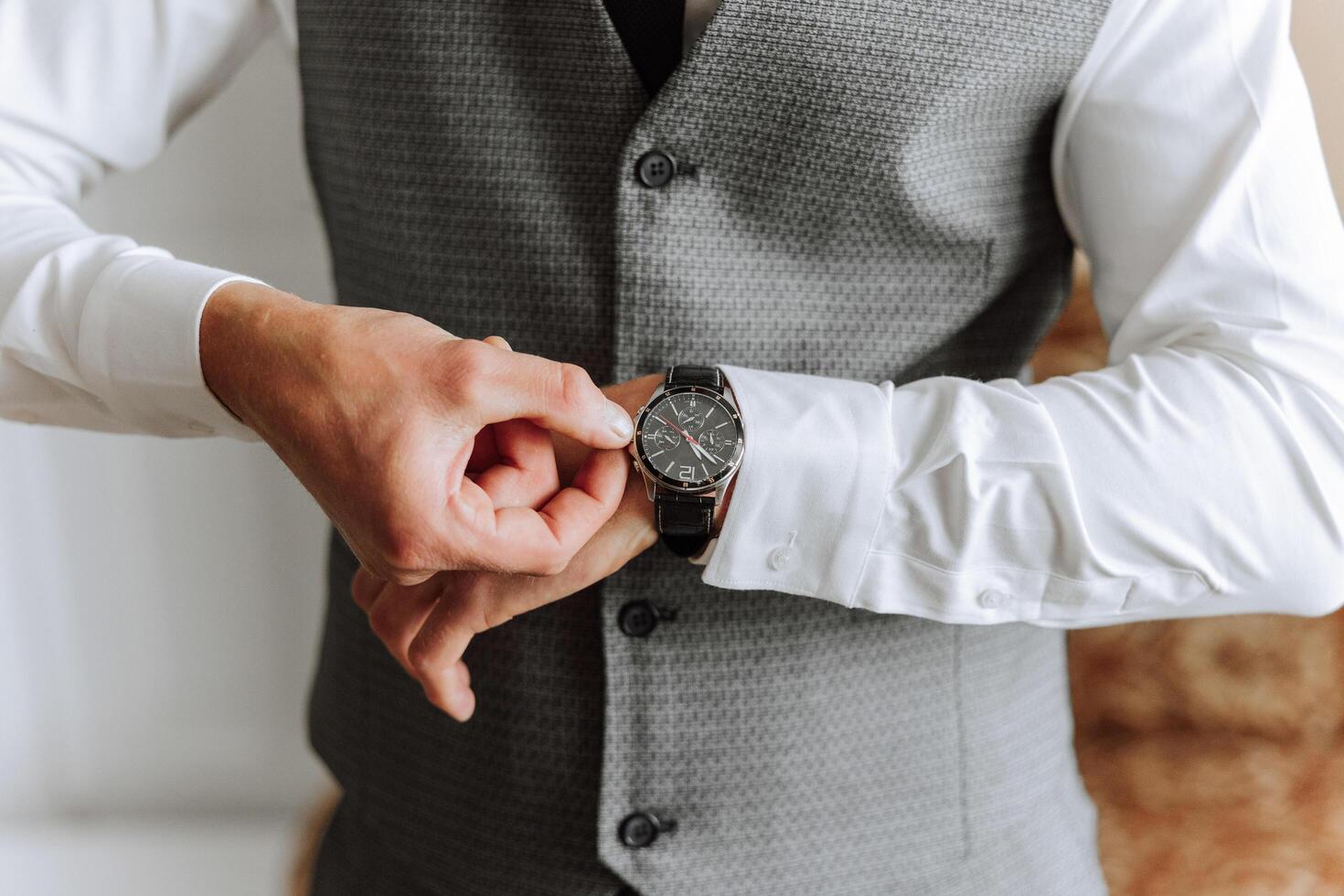 A man in a business suit is adjusting his wristwatch, a mug of coffee is on the table in his room. Close-up photo of a wristwatch.