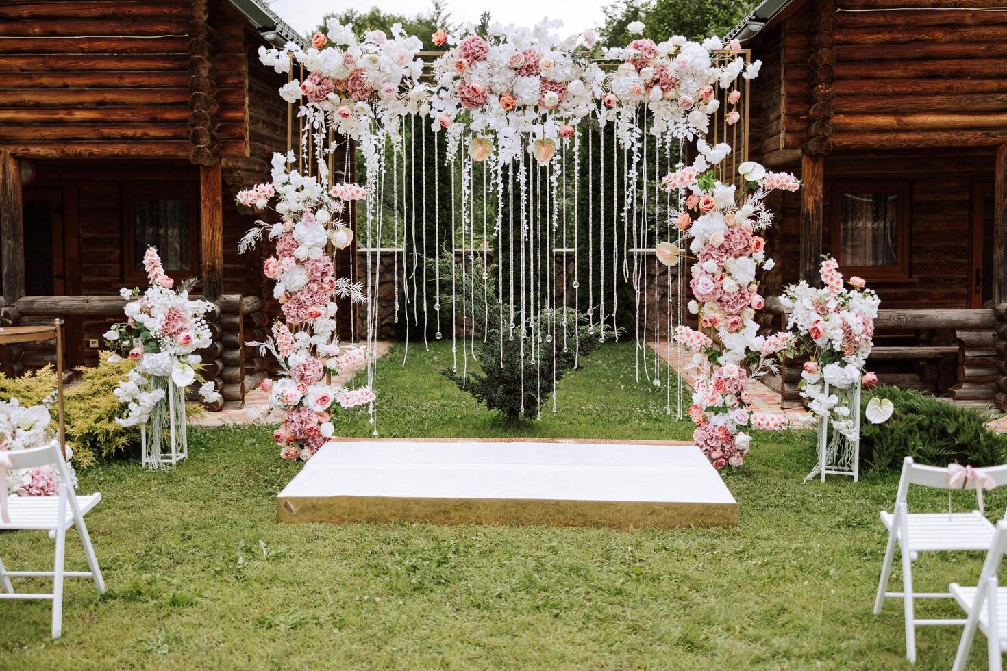 golden arch decorated with flowers on the background of trees. A white path that leads to the arch, many white chairs. Preparation for the wedding ceremony photo