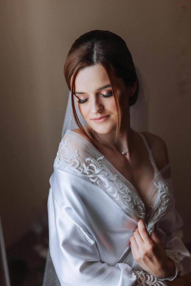 Beautiful bride in a dressing gown in the morning before the wedding ceremony. Incredible hairstyle of the bride. Natural and modern makeup. Portrait of a young bride in a dressing gown. photo