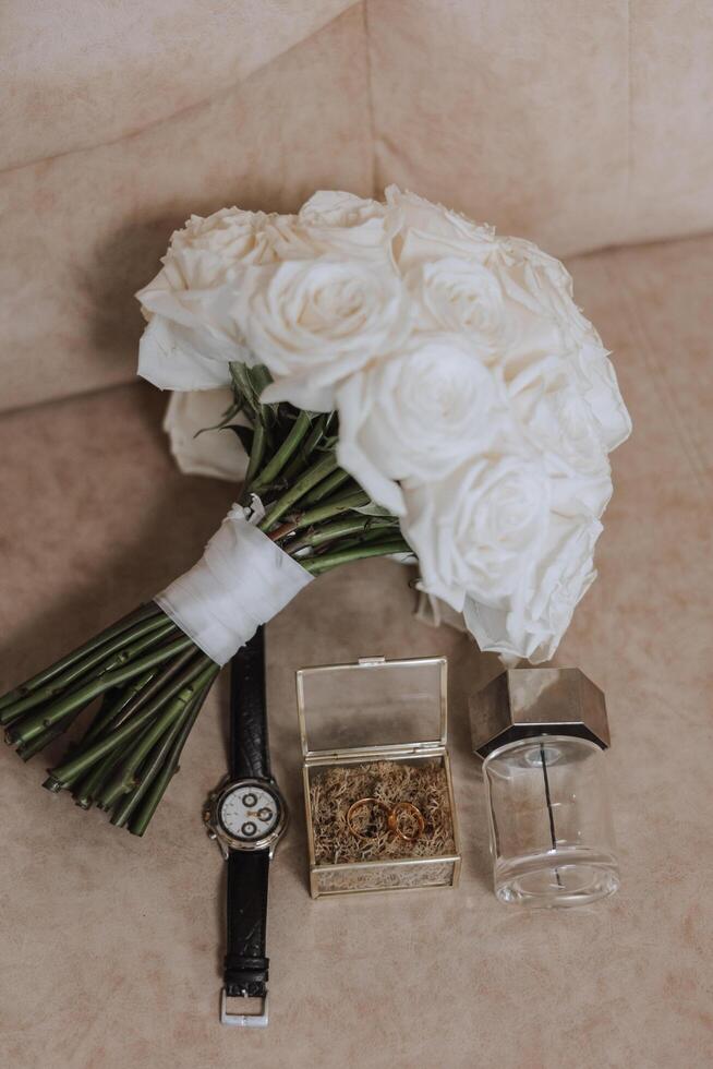 On the floor are men's dark leather shoes and a black belt, a man's suit on a mannequin, a wedding bouquet of flowers, wedding rings, men's perfume. Photo, top view. photo