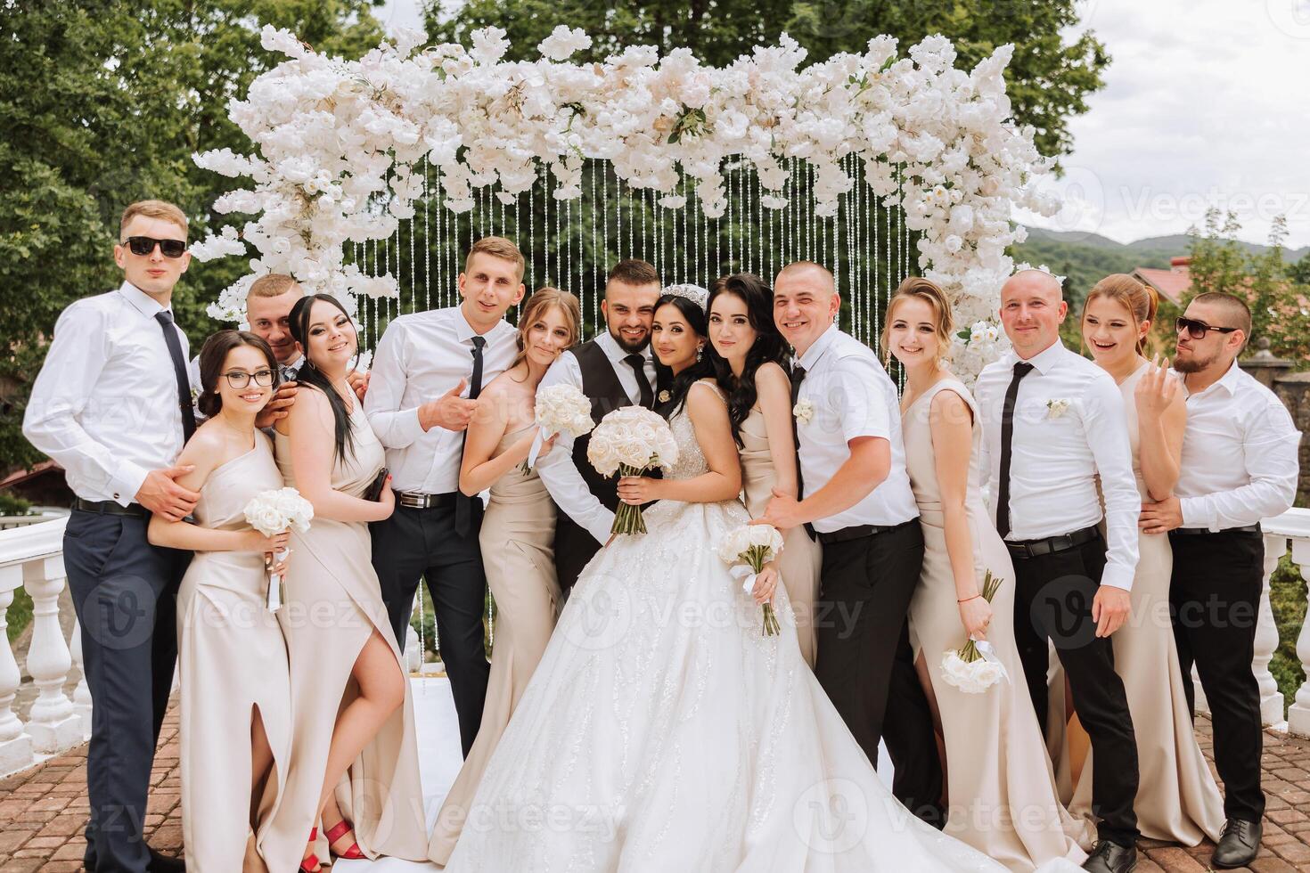The bride and groom and their friends pose near the arch. Long train of the dress. Stylish wedding. Summer wedding in nature photo