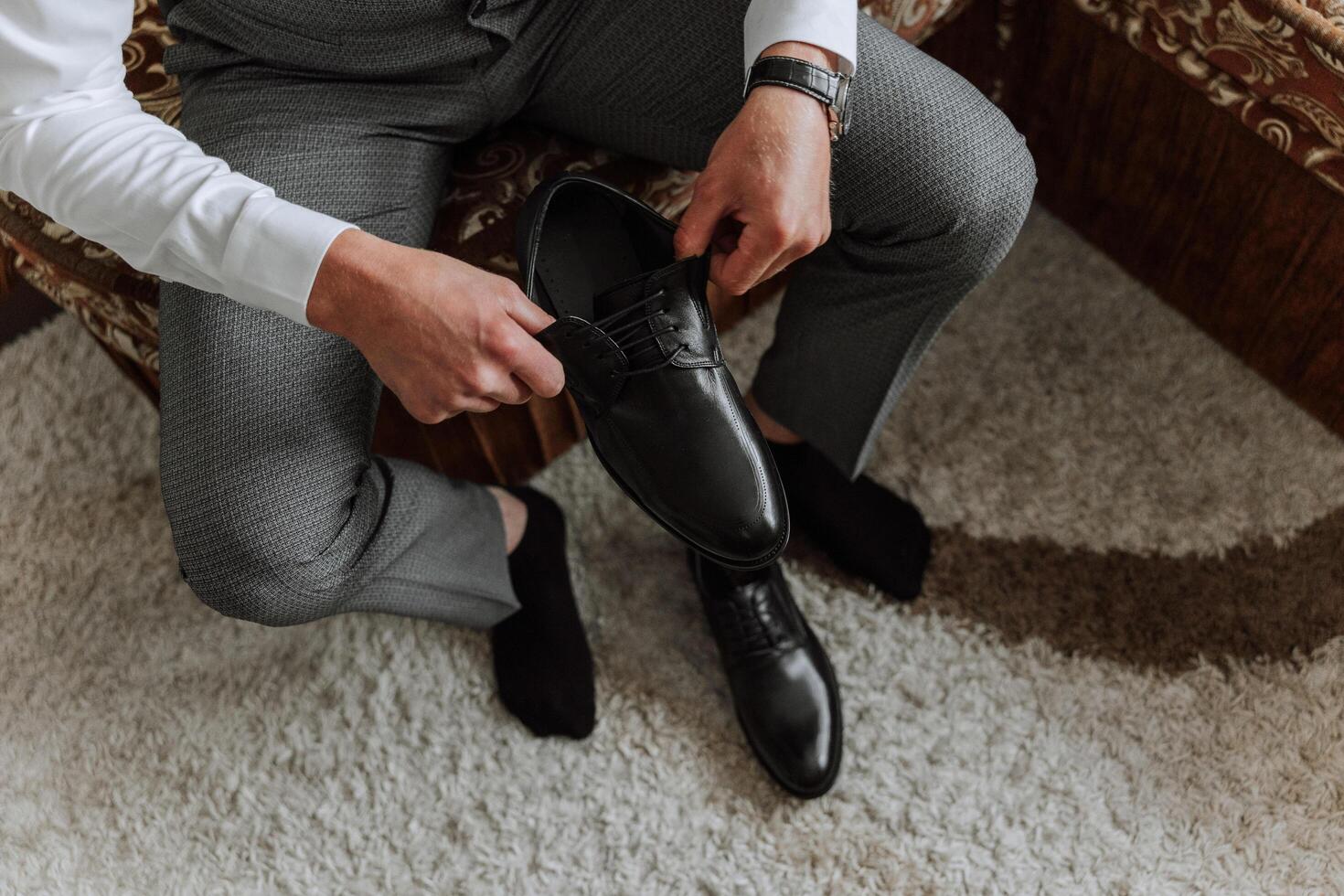 A young man put on black leather boots indoors. Close-up photo. Detail of a groom putting on his shoes photo