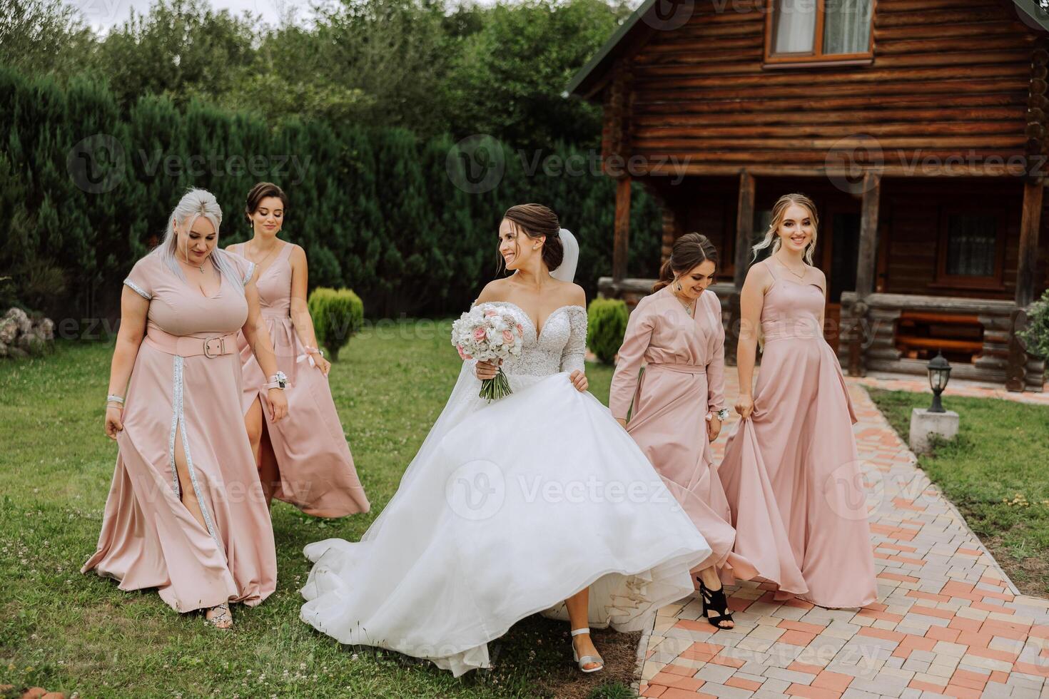 A brunette bride and her bridesmaids in identical pink dresses are walking against the background of nature. Girls in identical dresses are making out at a wedding. Wedding in nature. photo