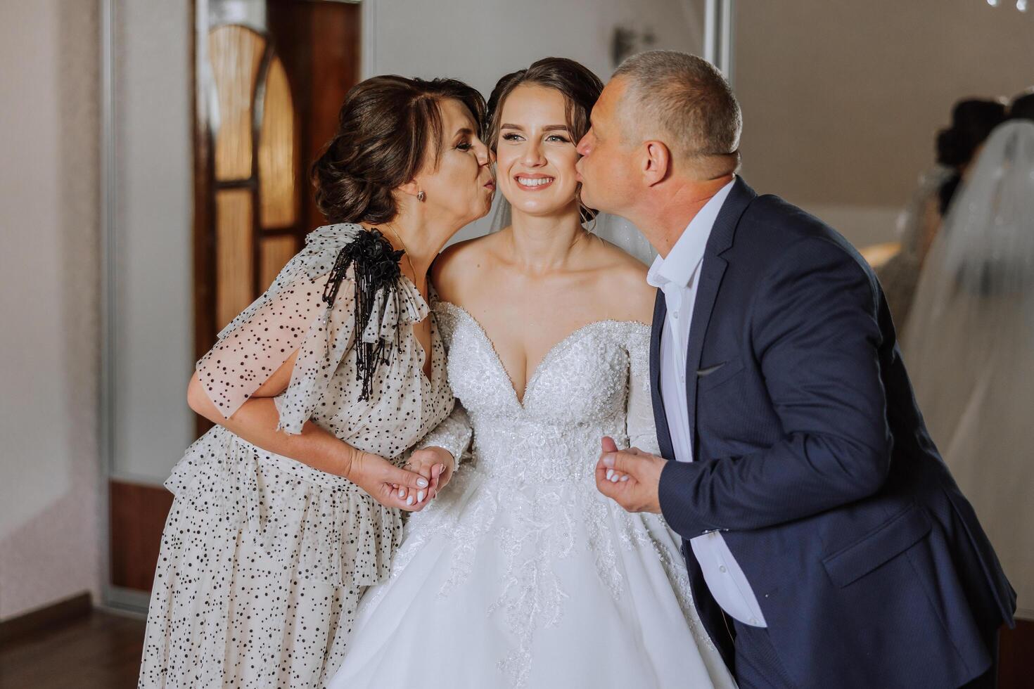 Happy parents hold the hands of the bride who is getting married and support her, wearing a wedding dress and a long veil. photo