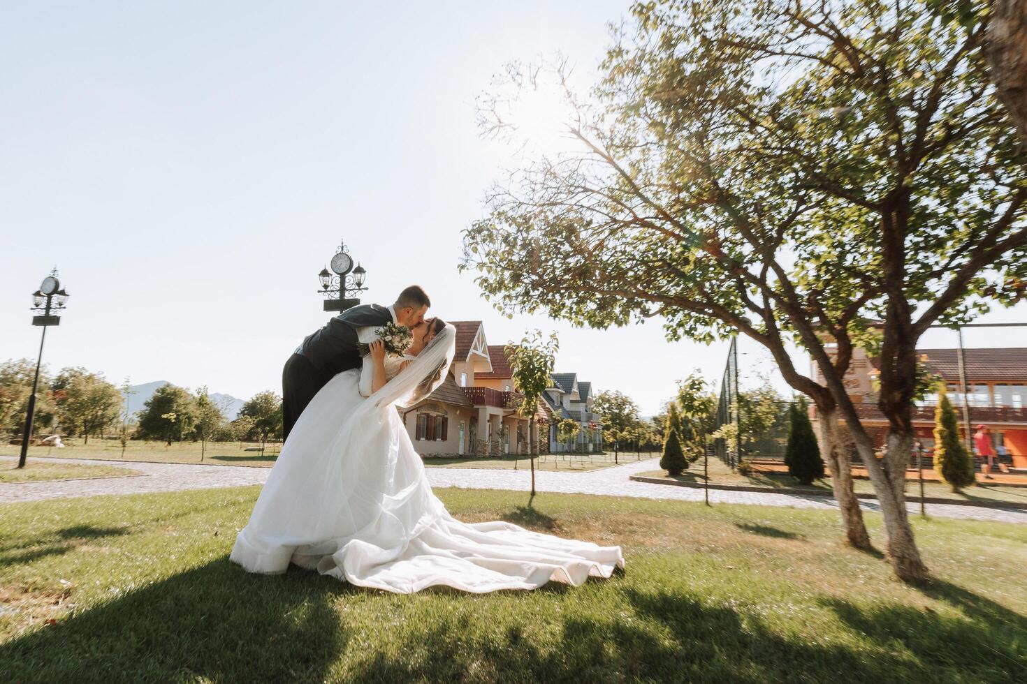 the groom passionately kisses the bride leaning her as if in a dance against the background of nature on a warm summer day. photo