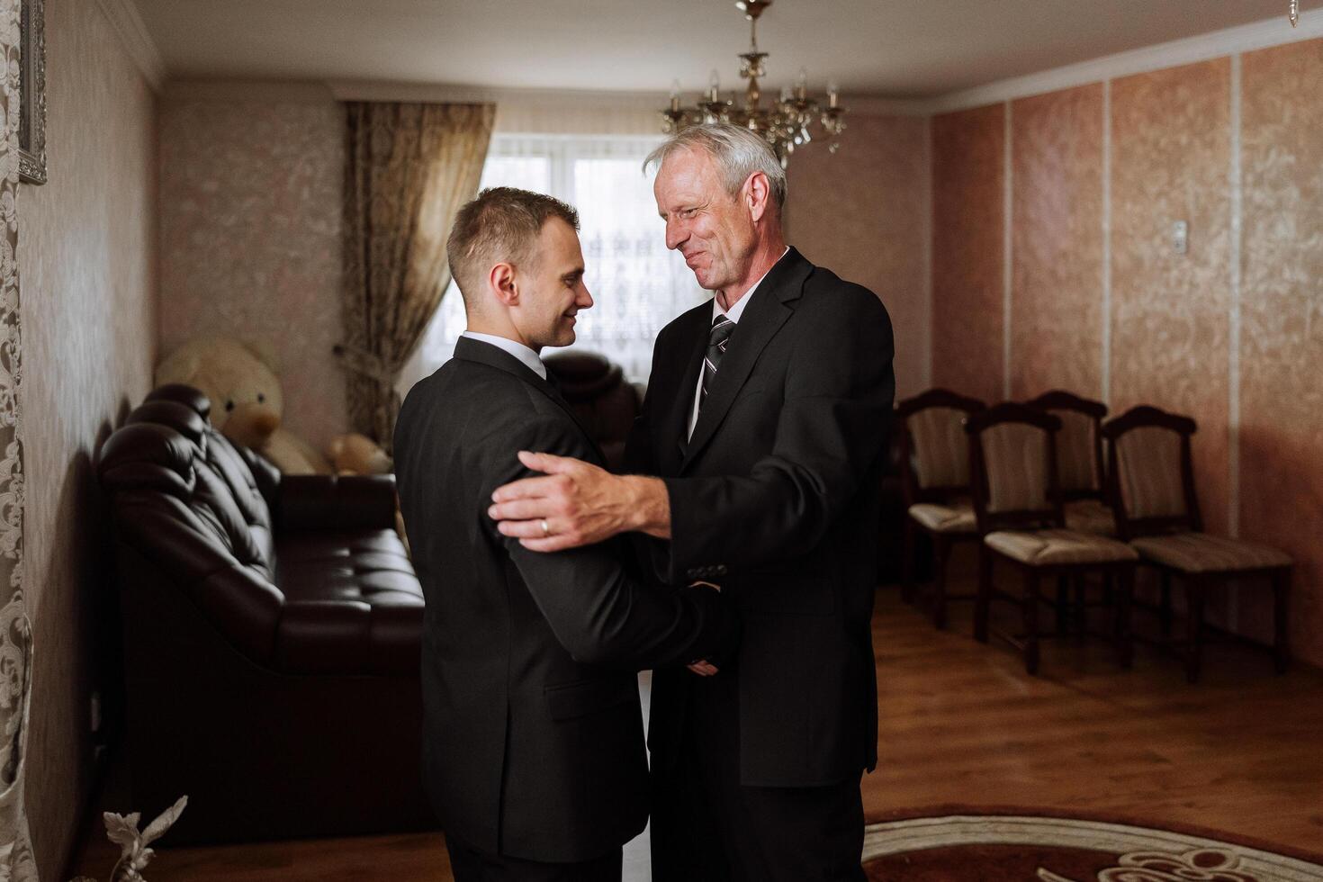 A father hugs his mature son and helps him prepare for the wedding ceremony. Warm and sincere relations between a father and an adult son. An emotional moment at a wedding photo