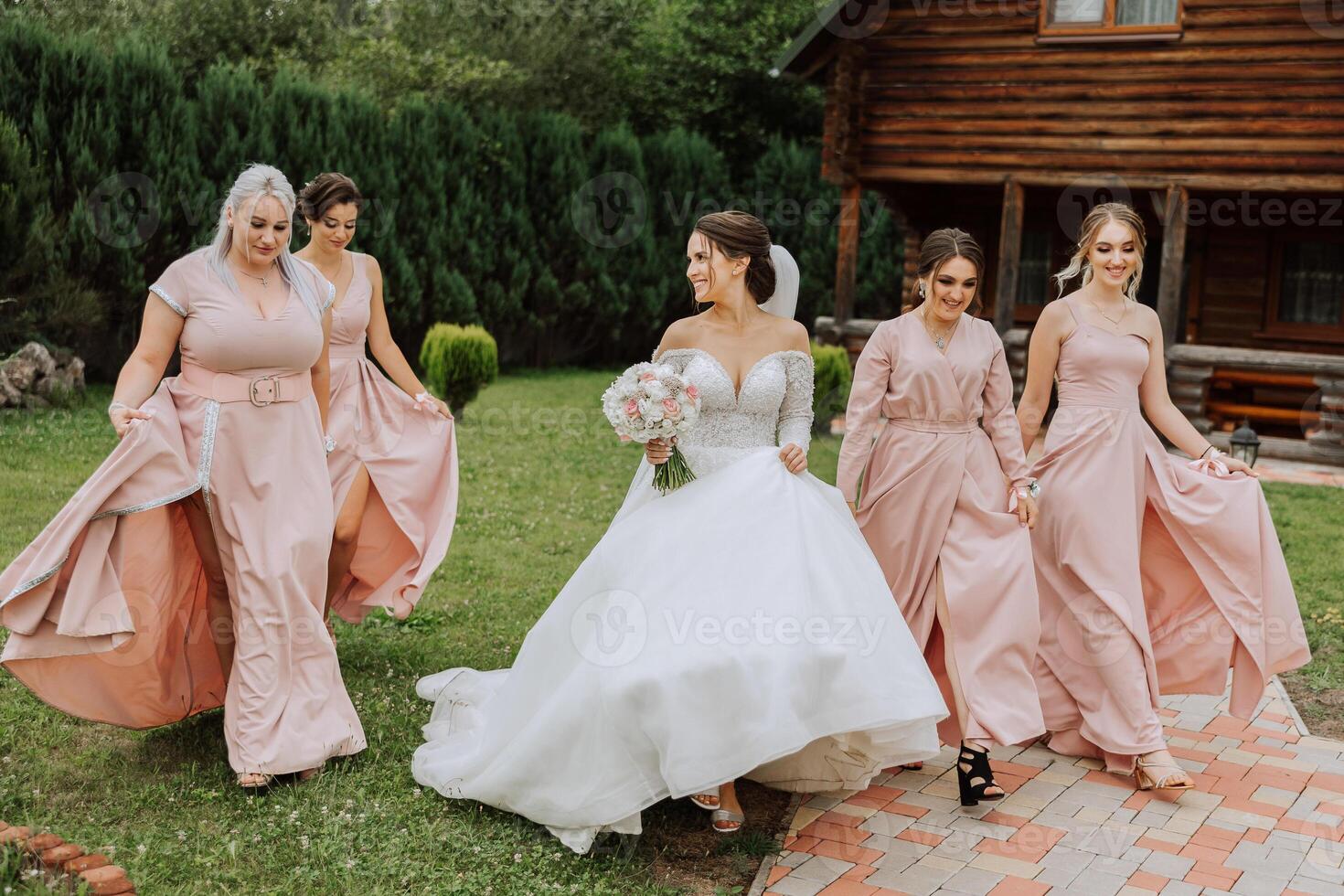 A brunette bride and her bridesmaids in identical pink dresses are walking against the background of nature. Girls in identical dresses are making out at a wedding. Wedding in nature. photo