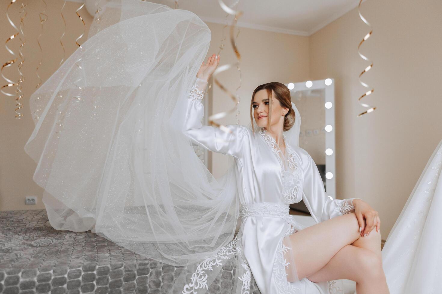 A beautiful bride is sitting in a dressing gown in the morning before the wedding ceremony in a hotel with a modern interior. Incredible hairstyle of the bride. Natural and modern makeup. photo