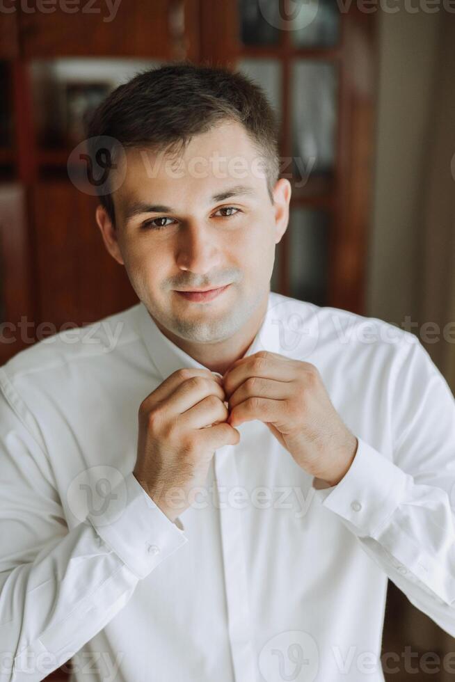 Business shirt. A man in a white shirt fastens the buttons. Young politician, male style, businessman buttoning shirt, male hands close-up, american, european businessman photo