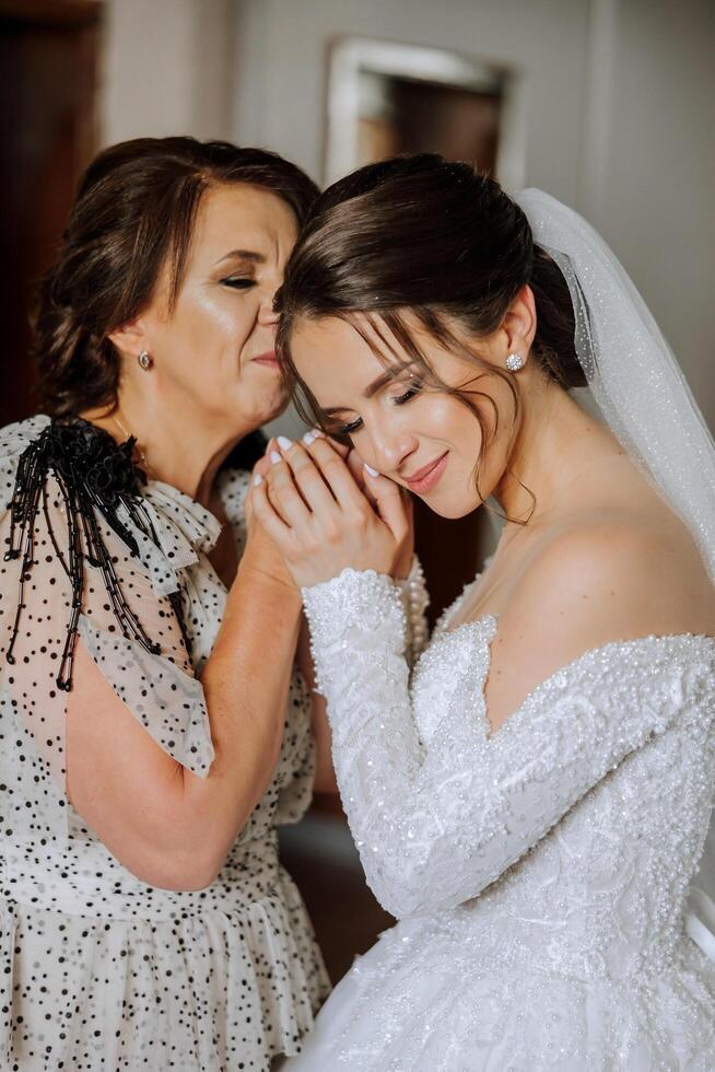 A beautiful and happy mother and her daughter, the bride, are standing next to each other. The best day for parents. Tender moments at the wedding. photo