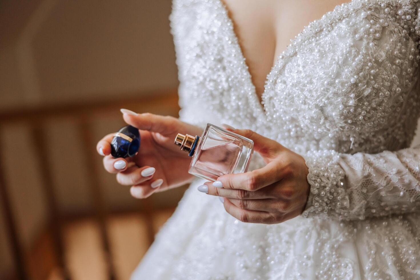 Pink perfume bottle in tender female hands. The bride sprays perfume on her body. Close-up photo. Manicure. Morning of the bride. photo