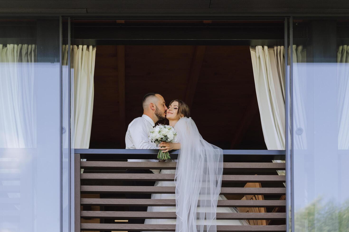 un recién casado Pareja. el viento ascensores un largo blanco velo en verano. el novia y novio son abrazando, un largo velo es soplo en el viento. el recién casados Beso en el balcón de el restaurante foto