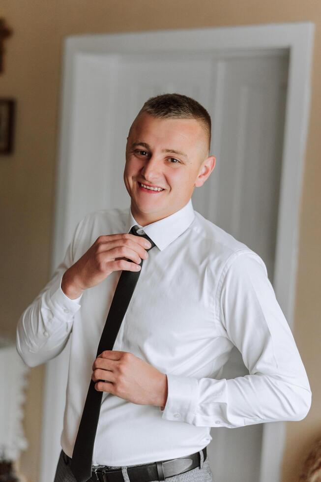 man in shirt dressing up and adjusting tie on neck at home. Wedding day concept,fashion, business, male style. photo