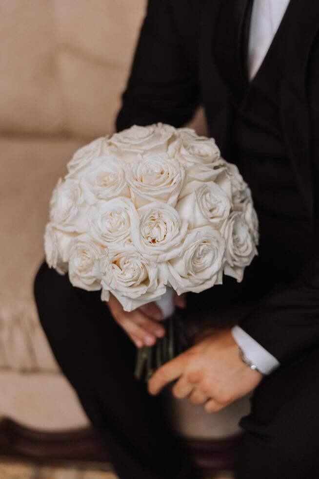 Wedding bouquet. White cut roses, green seed heads and leaves. Green stems and white ribbon and gold wedding rings. photo