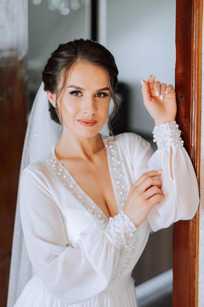 Beautiful bride in a dressing gown in the morning before the wedding ceremony. Incredible hairstyle of the bride. Natural and modern makeup. Portrait of a young bride in a dressing gown. photo