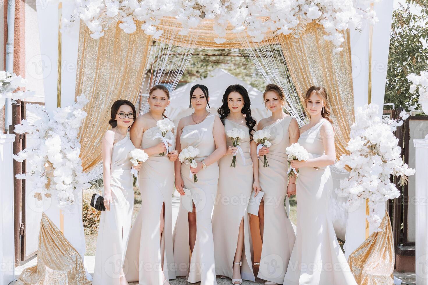 a group of beautiful girls in identical dresses with flowers, near an arch decorated with flowers. Summer photo. photo