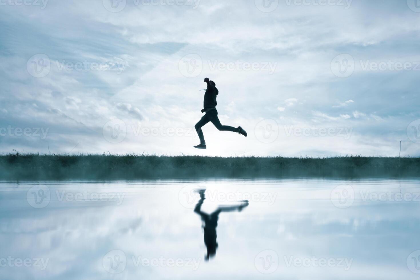 man jumping in the field and reflecting in the lake photo