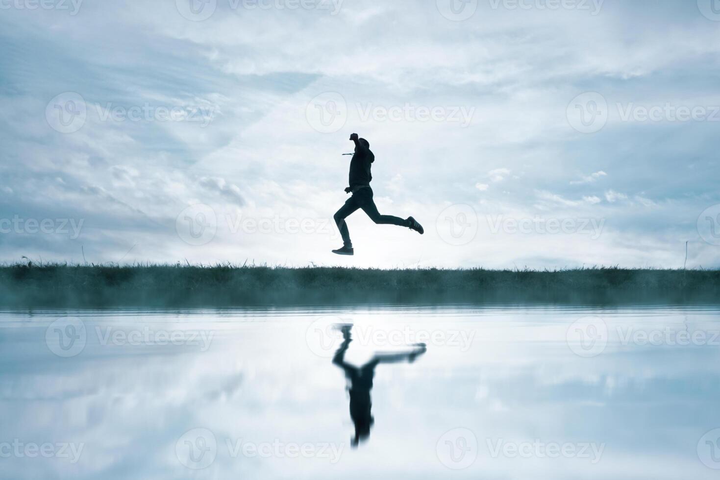 man jumping in the field and reflecting in the lake photo