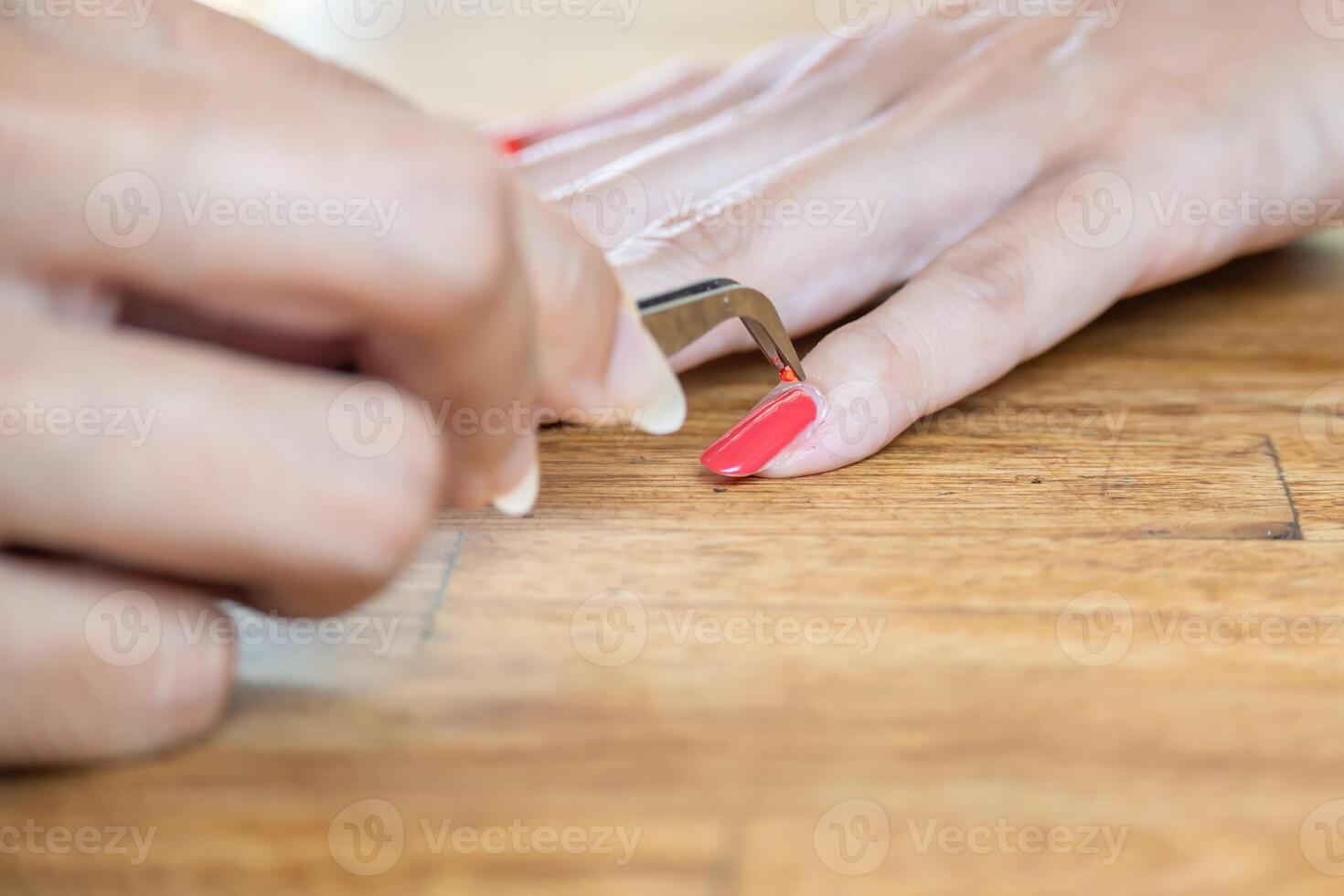 Woman's hands with a tweezer for applying nail accessory. She is applying a little red glitter on her nail. photo
