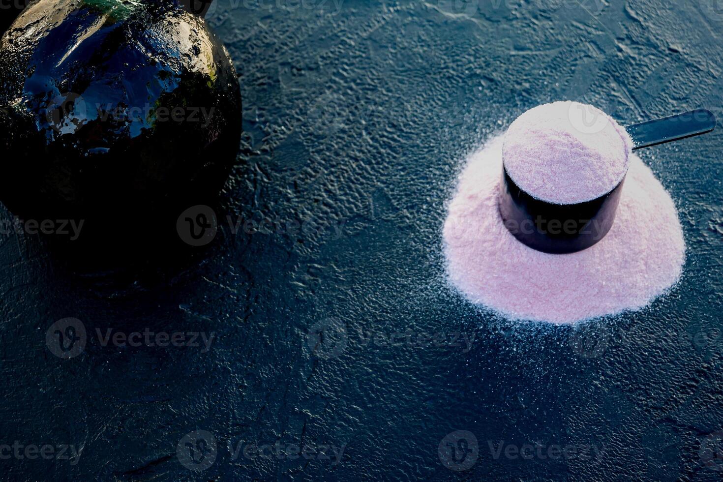 Scoop of creatine on a black table accompanied by a kettlebell. photo