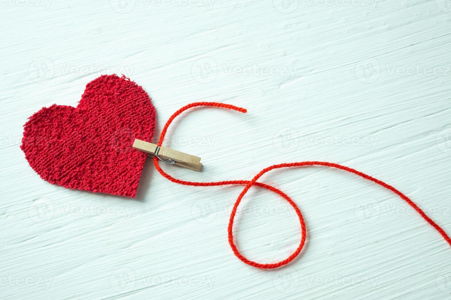 felpa corazón atrapado por un pinza de ropa con un rojo hilo en un blanco de madera mesa. foto