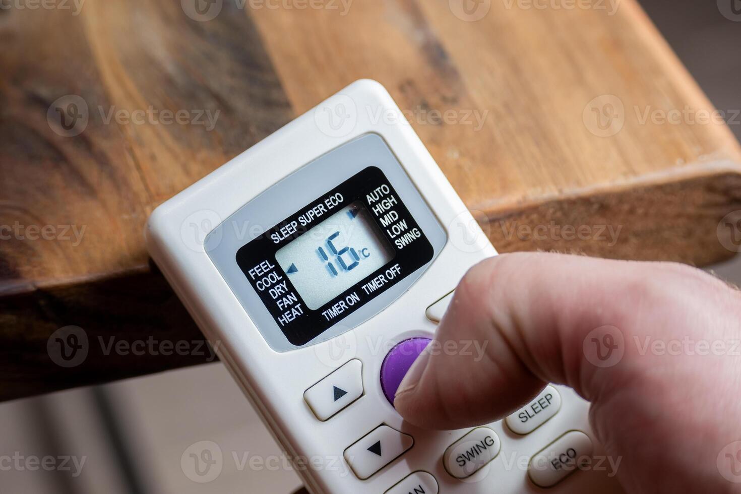 Finger of a man using the control of an air conditioner that reads sixteen degrees. photo