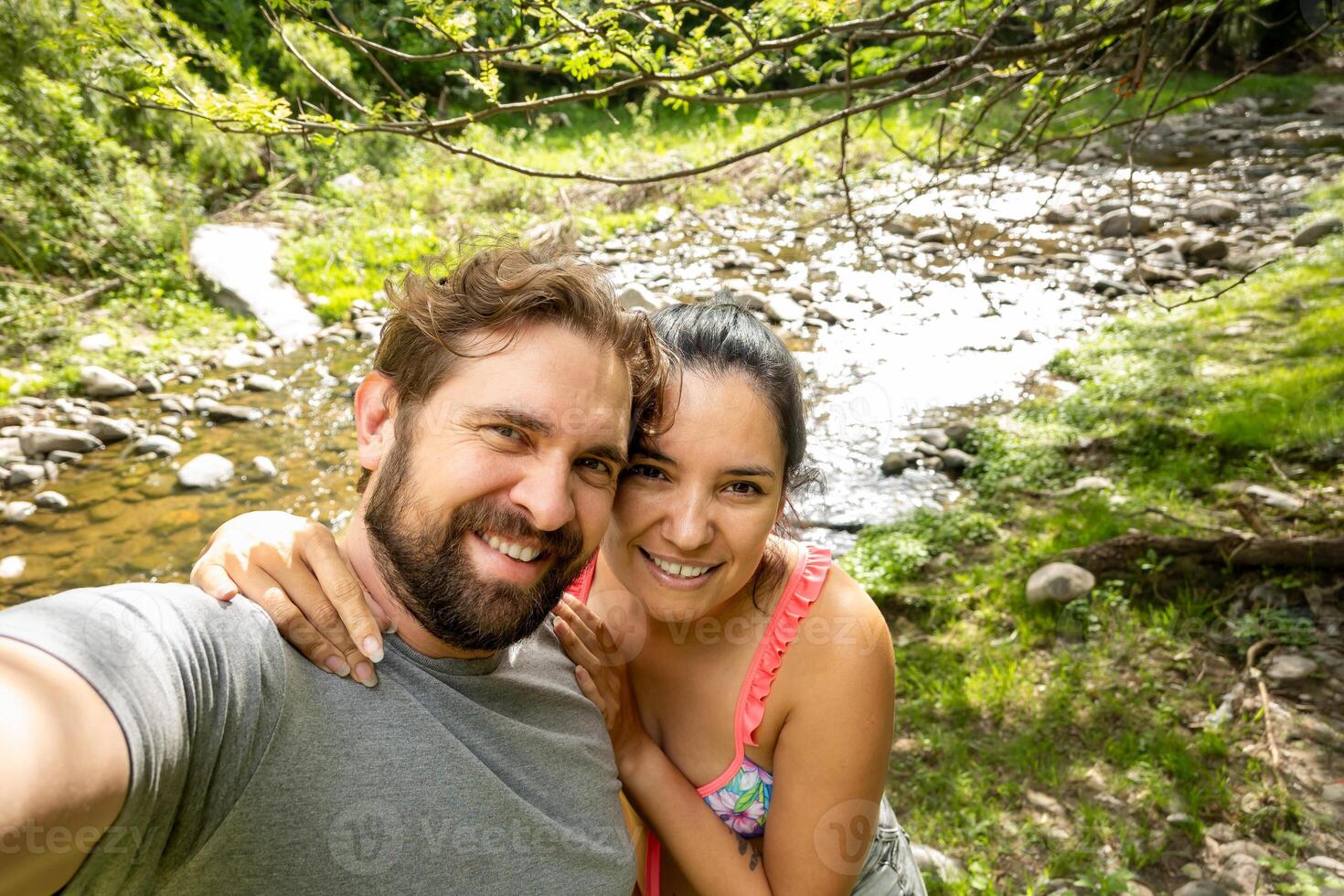 Latin woman and man take a selfie in a natural environment, where a river passes, they are smiling and in love. photo