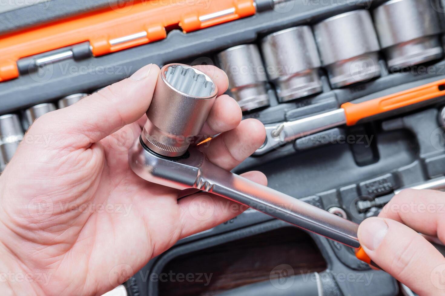 Hands of a man holding a ratchet wrench in the background you can see the toolbox. photo