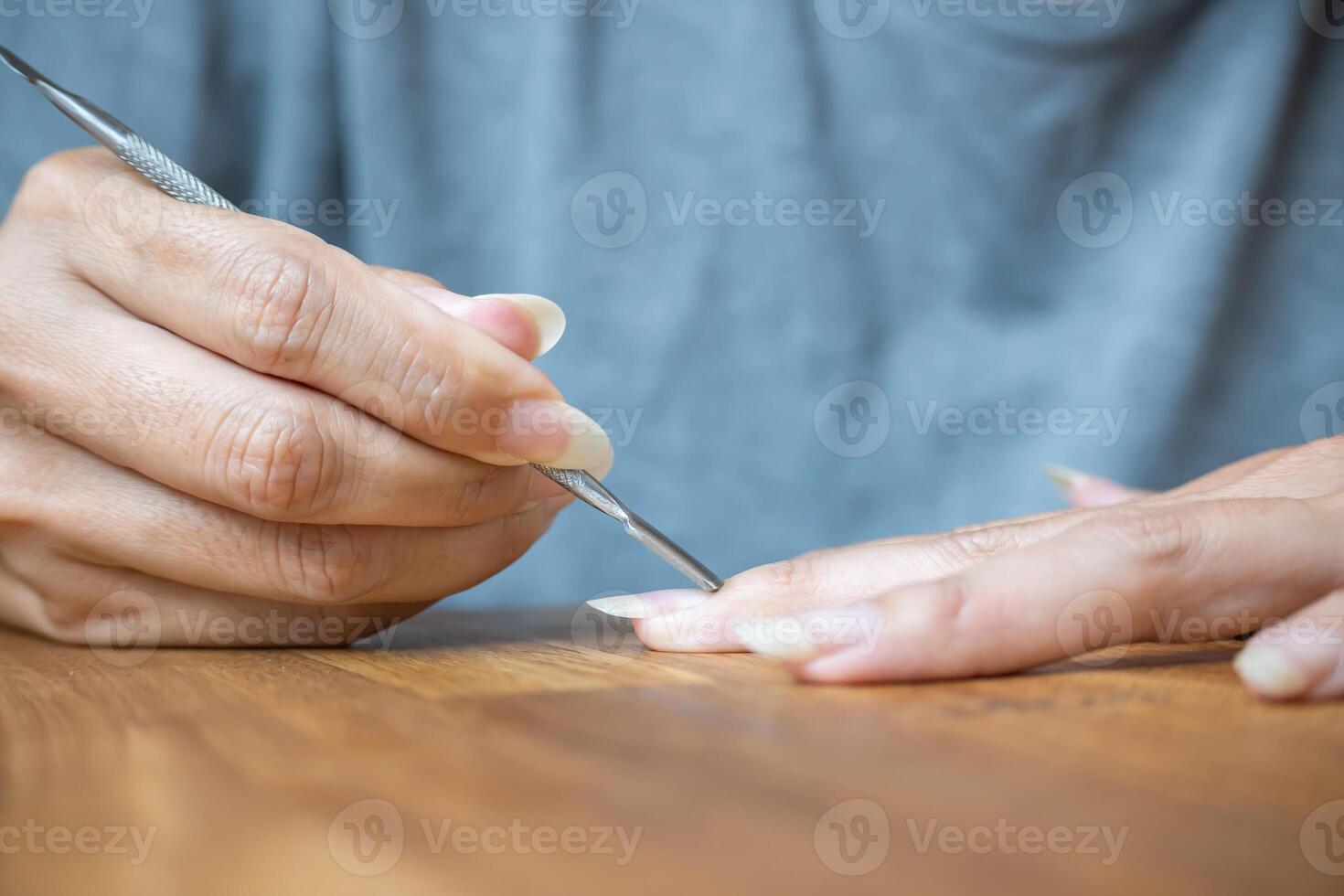 Woman using a cuticle pusher on her nails. Nail preparation process before applying polish. photo
