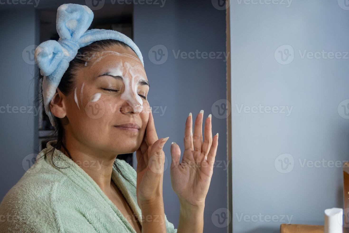 latín niña aplica limpieza espuma en su rostro. foto