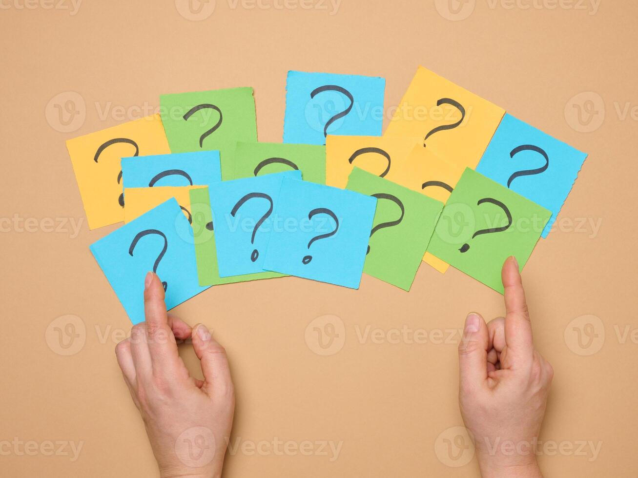 Female hands hold paper sheets with a drawn question mark on a beige background photo