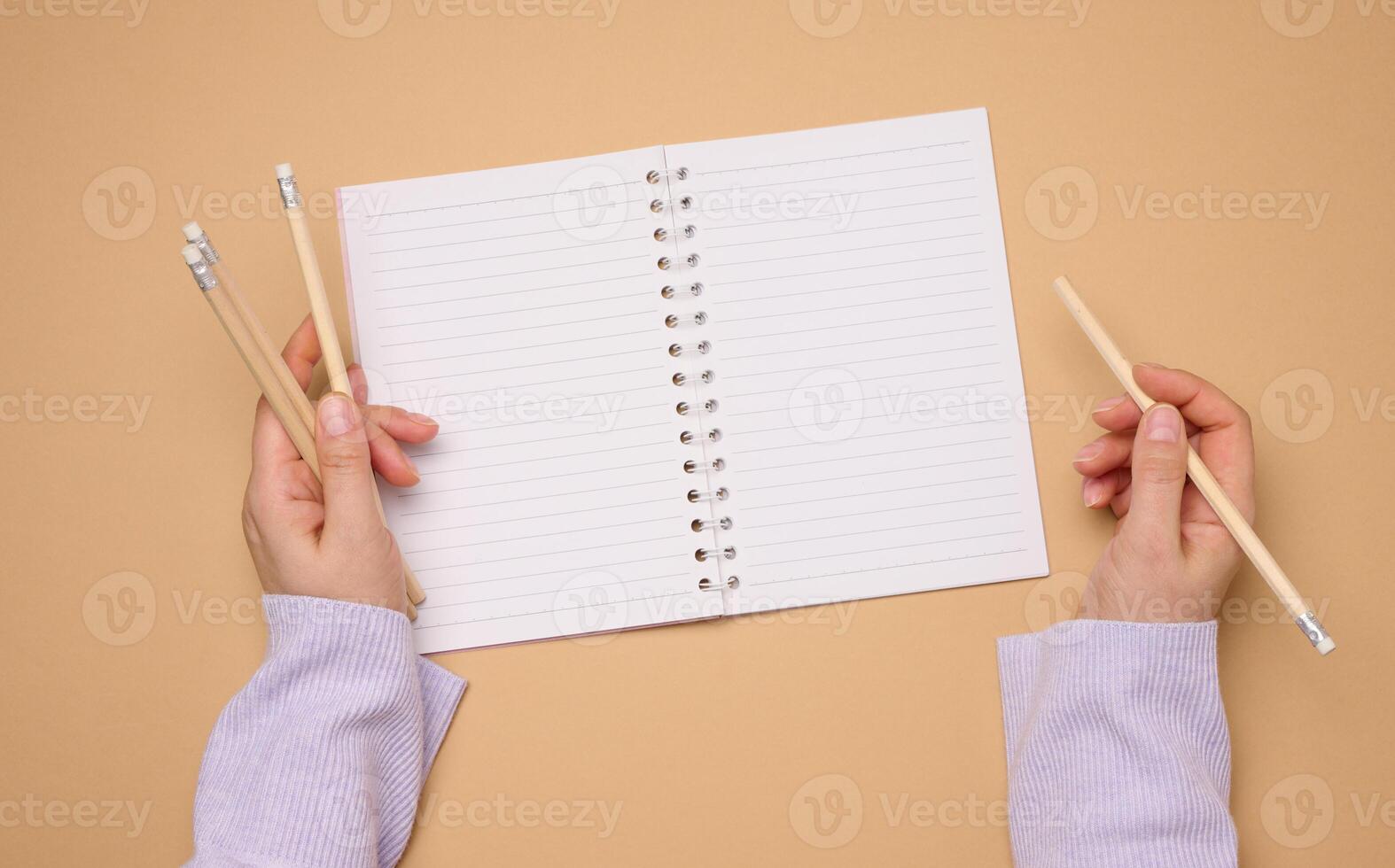 Open notebook with empty white sheets and a woman's hand holding a wooden pen on a yellow background photo