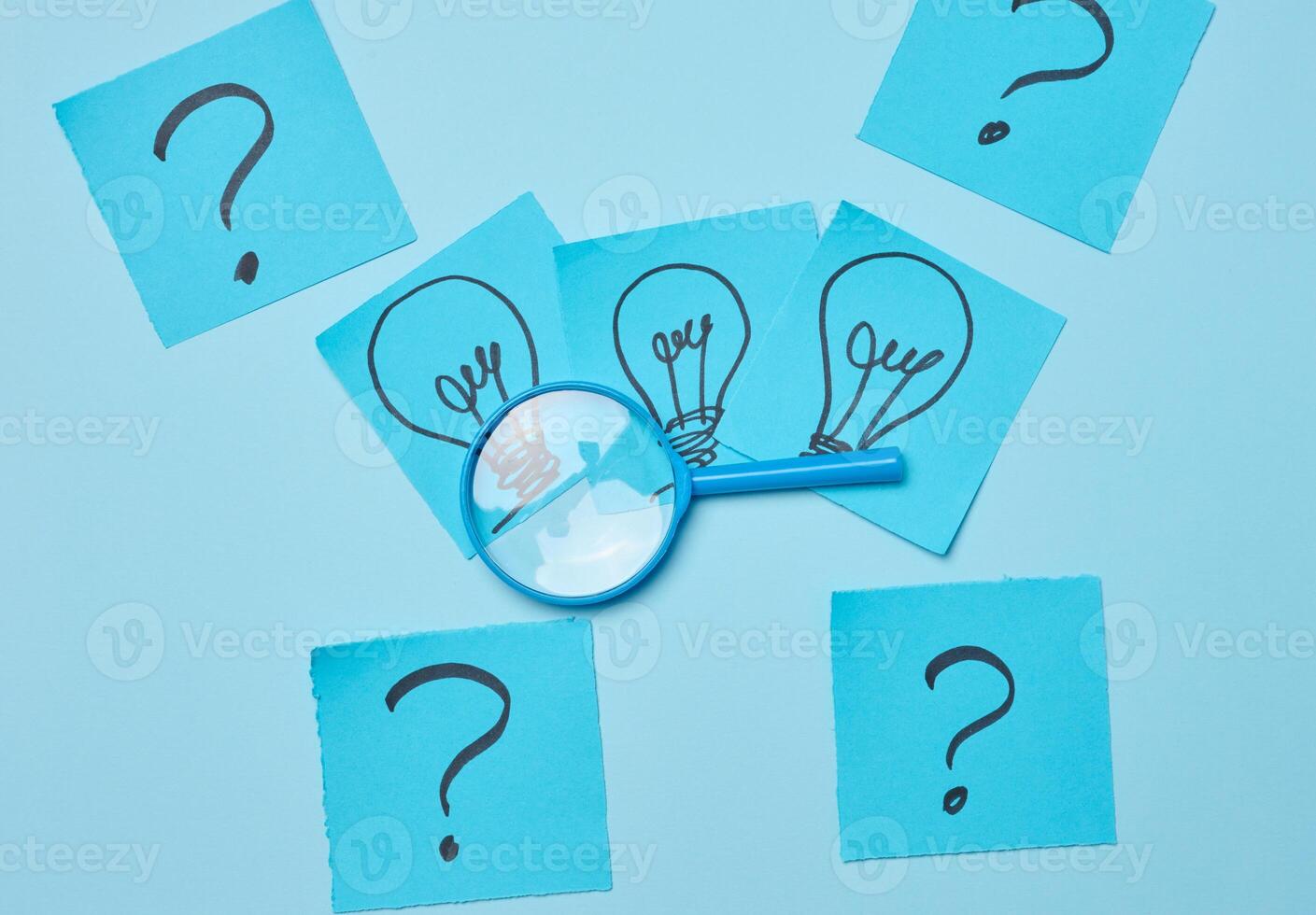 Drawn light bulbs on sheets of paper and a plastic magnifying glass photo