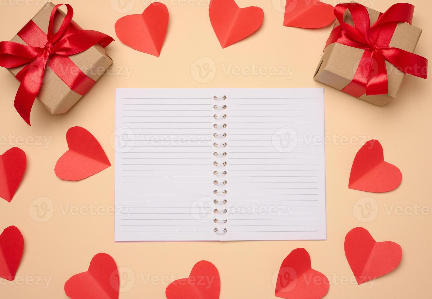 Open notebook with empty white sheets, red hearts and gift boxes on a beige background photo
