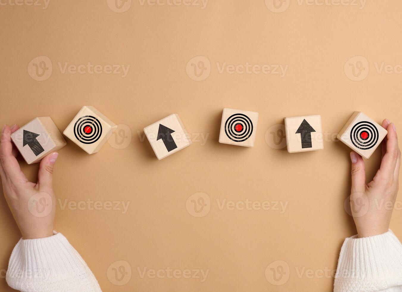 A woman's hand holds wooden cubes with arrows and a drawn target photo