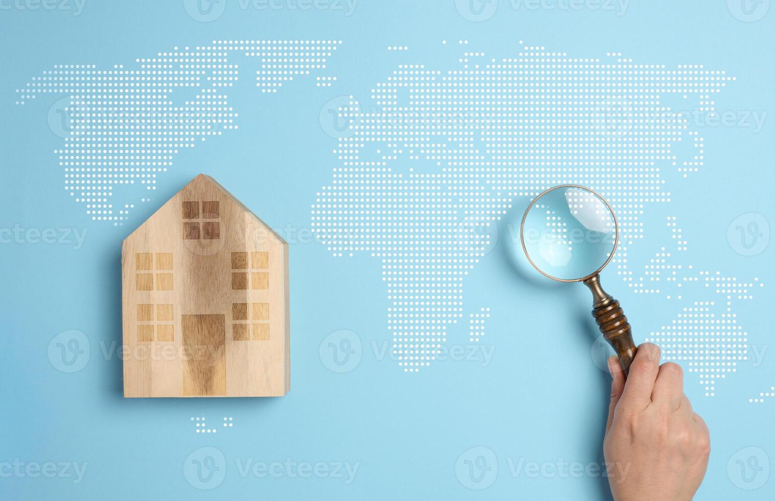 Wooden house on a world map background with a person's hand holding a magnifying glass photo