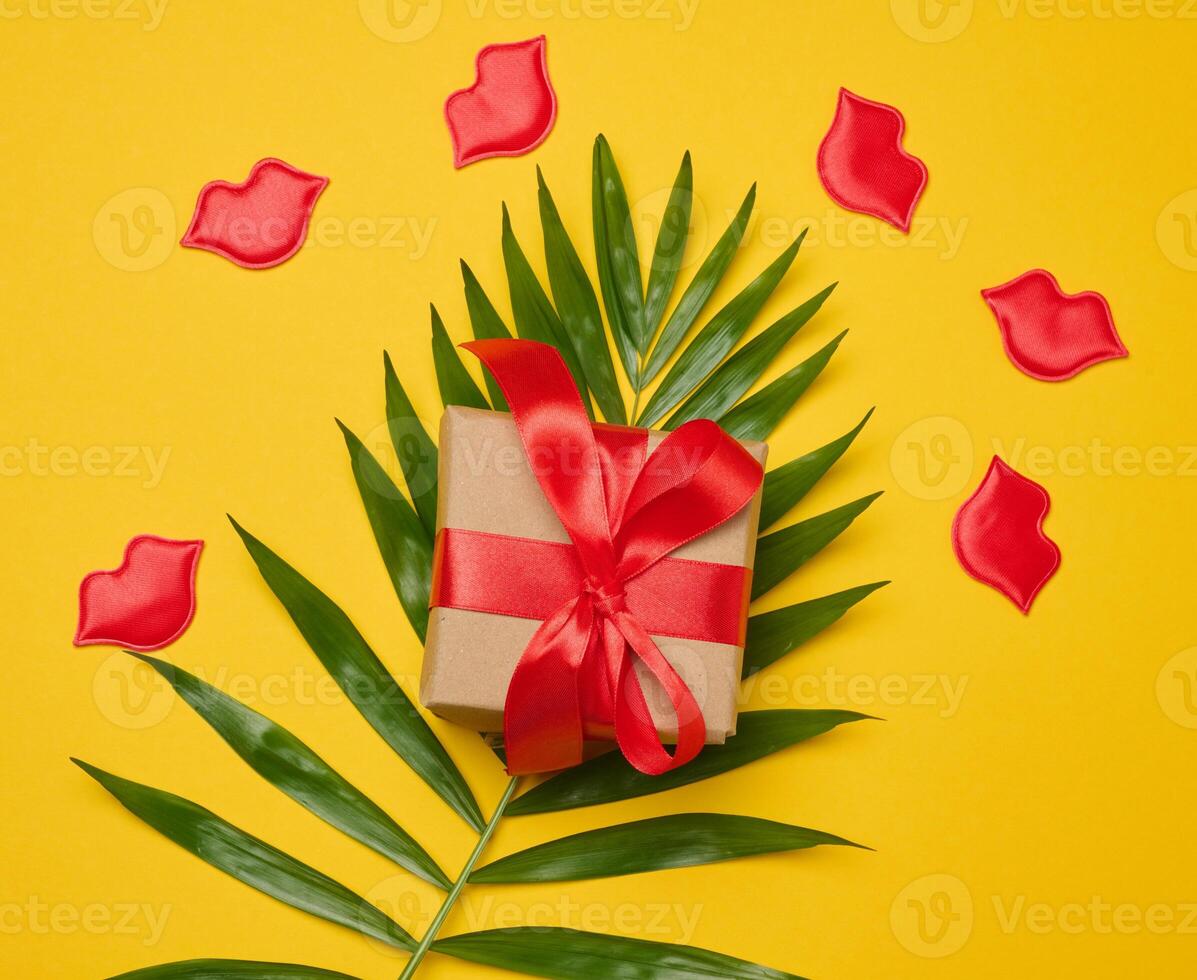 Gift box with red satin ribbon and bow on a yellow background. photo