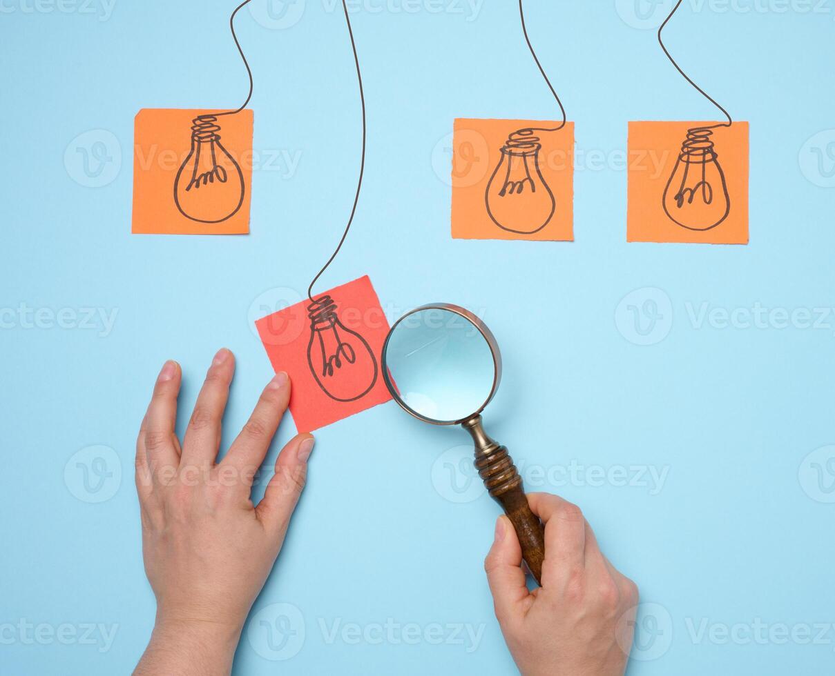 Drawn electric lamps on stickers, concept of searching for new ideas, brainstorming. Woman's hand holding a magnifying glass photo