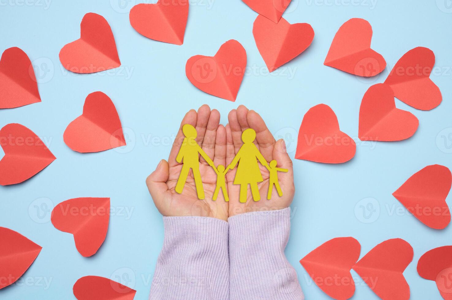 Woman's hand holding paper cut family with child, blue background photo