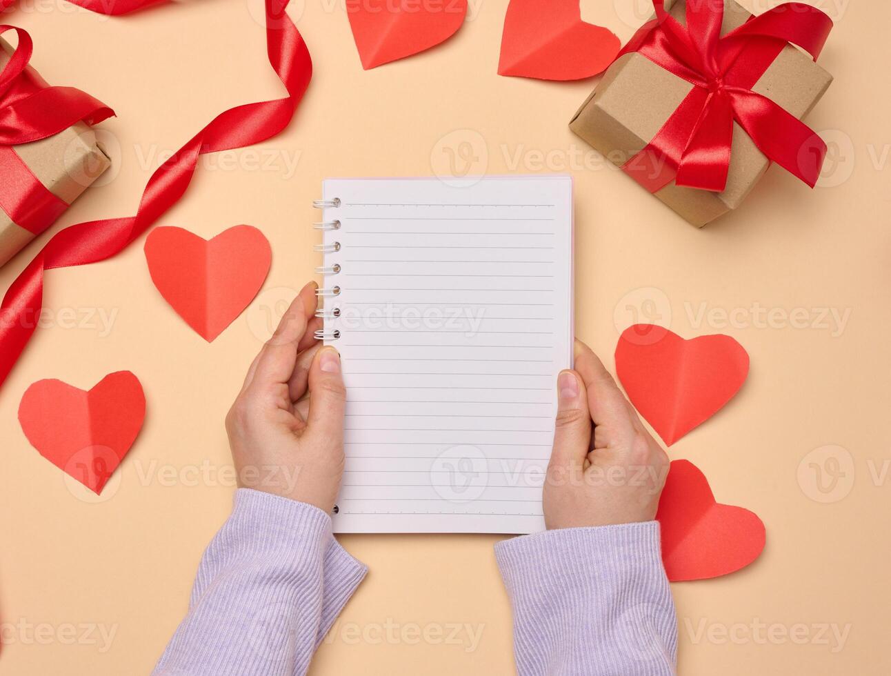 Open notebook with empty white sheets and gift boxes around on a yellow background, top view. photo