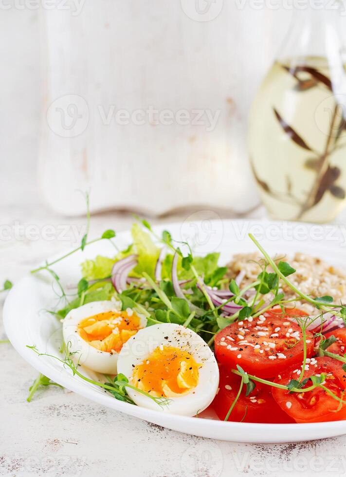 Breakfast oatmeal porridge with boiled eggs and fresh vegetables. Healthy balanced food. Trendy food. photo